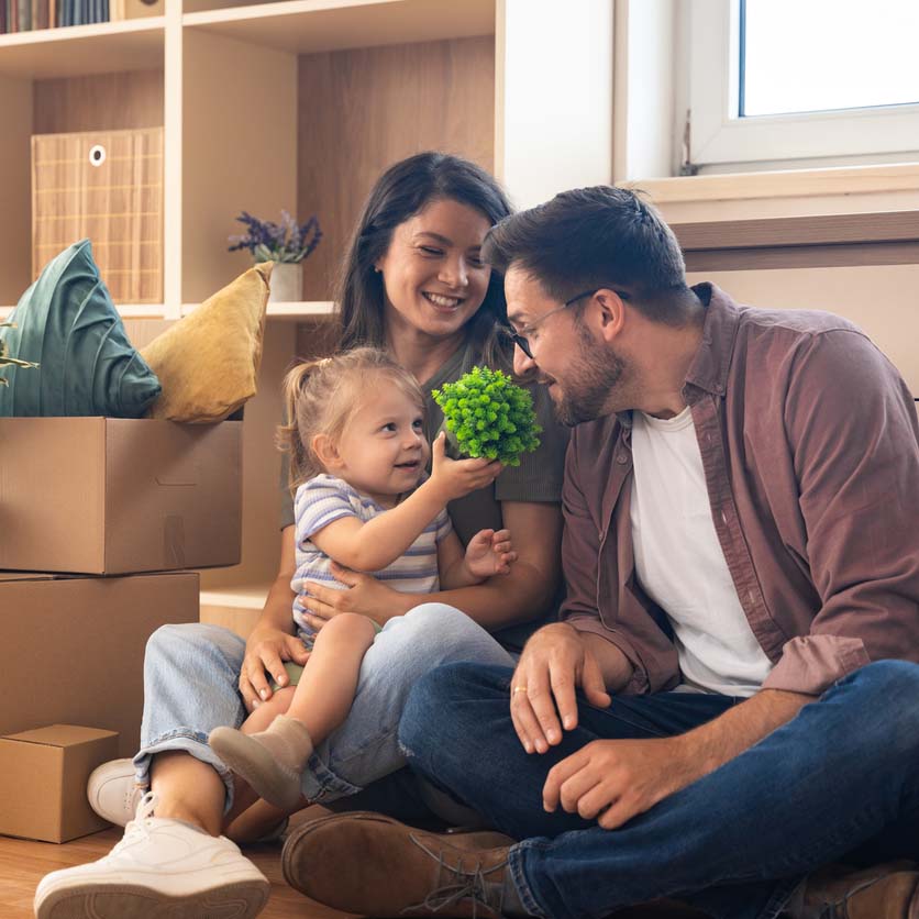 Happy family moving into new home. Young man and woman, parents of small baby girl, having fun with their child, while unpacking cardboard boxes starting their new independent life at new apartment.